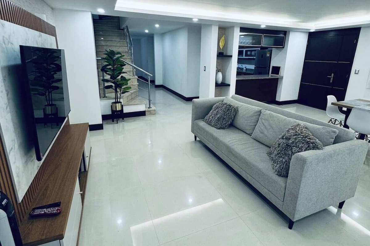 Ein modernes Wohnzimmer mit einem grauen Sofa, einem Fernseher und einer Treppe, die zu einer weiteren Ebene führt.