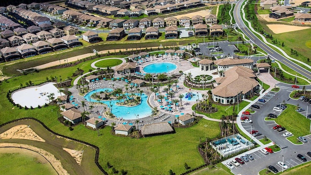 Vue aérienne d’un quartier résidentiel comprenant un grand complexe de piscines, de nombreuses rues et un parking.