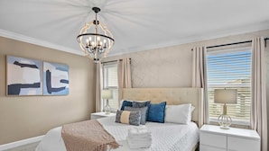 Une chambre à coucher bien aménagée, avec un grand lit, un lustre et des œuvres d’art accrochées au mur.