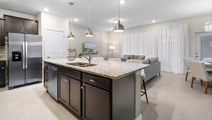 Una cocina moderna con una isla central, electrodomésticos de acero inoxidable, iluminación colgante y un comedor con sofá y sillas.