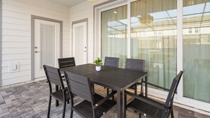 Un comedor con mesa y sillas de madera oscura, una planta en maceta y un amplio ventanal corredero.