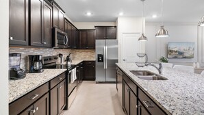 Una cocina moderna con armarios de madera oscura, electrodomésticos de acero inoxidable, encimeras de granito e iluminación colgante.