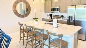 A modern kitchen with a large island, stainless steel appliances, and wooden chairs. - Reunion resort (7 guests) near Disney (Kissimmee)