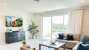 A spacious living room with a large flat-screen TV, a sofa, a coffee table, and a dining area with a table and chairs. - Reunion resort (7 guests) near Disney (Kissimmee)