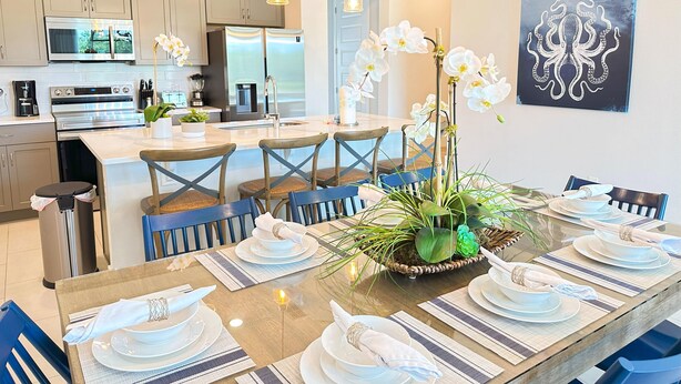 A modern kitchen with stainless steel appliances, a dining area with a glass table set for six, and a large orchid centerpiece. - Reunion resort (7 guests) near Disney (Kissimmee)