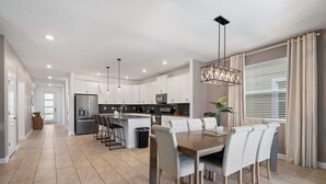Une cuisine moderne avec des meubles blancs, un îlot central et un coin repas comprenant une table et des chaises en bois.