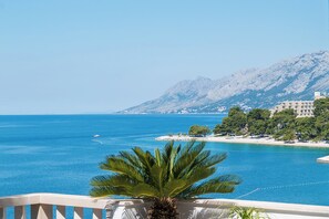A coastal view with a clear blue sea, a mountain in the background, and a building with a balcony overlooking the water. - 2BR Apartment with balcony and sea view (Brela)
