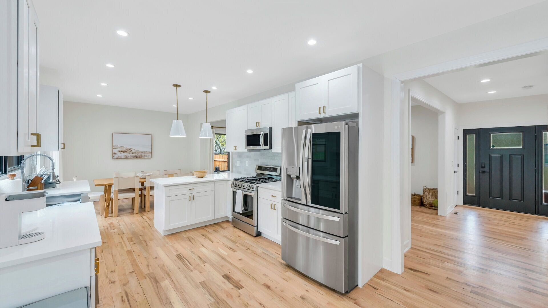 Une cuisine moderne avec des meubles blancs, des appareils en acier inoxydable et un plancher en bois.