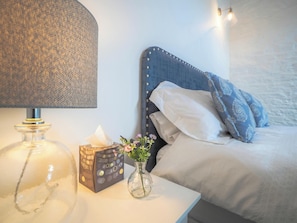 Een netjes opgemaakte slaapkamer met een bed, nachtkastje met een lamp, een vaas met bloemen en een decoratieve doos.