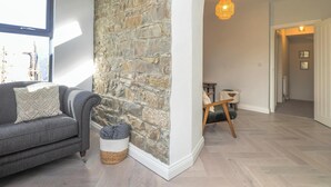 Une pièce avec un mur en pierre, un canapé gris, un panier en osier et un plancher en bois.