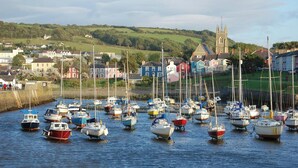 Un port où de nombreux bateaux sont amarrés, une église dotée d’un clocher et, au loin, des maisons aux couleurs vives.