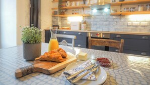 Une table dressée pour le petit-déjeuner avec des croissants, un verre de jus d’orange et une petite plante.