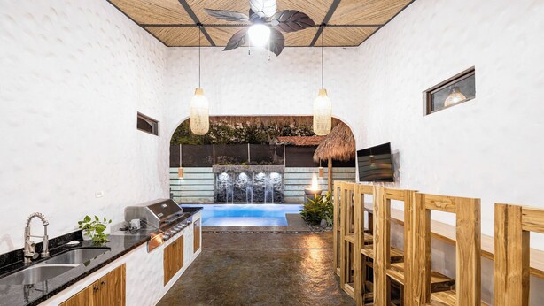 A modern kitchen with a built-in grill, a stone countertop, and a view of a backyard with a pool and waterfall. - Luxury Retreat Villa private Pool & BBQ by SPCR (Potrero)