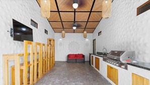 A modern kitchen with a built-in grill, wooden cabinets, and a seating area with a red sofa. - Luxury Retreat Villa private Pool & BBQ by SPCR (Potrero)