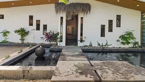 A modern building with a thatched roof entrance, a water feature, and potted plants. - Luxury Retreat Villa private Pool & BBQ by SPCR (Potrero)