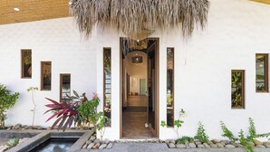 A building with a white exterior, a thatched roof entrance, and a water feature in front. - Luxury Retreat Villa private Pool & BBQ by SPCR (Potrero)