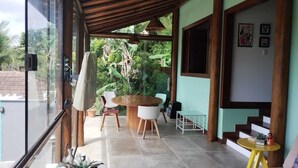 A covered outdoor area with a round table and chairs, a small table with a decorative item, and a staircase leading to an upper level.