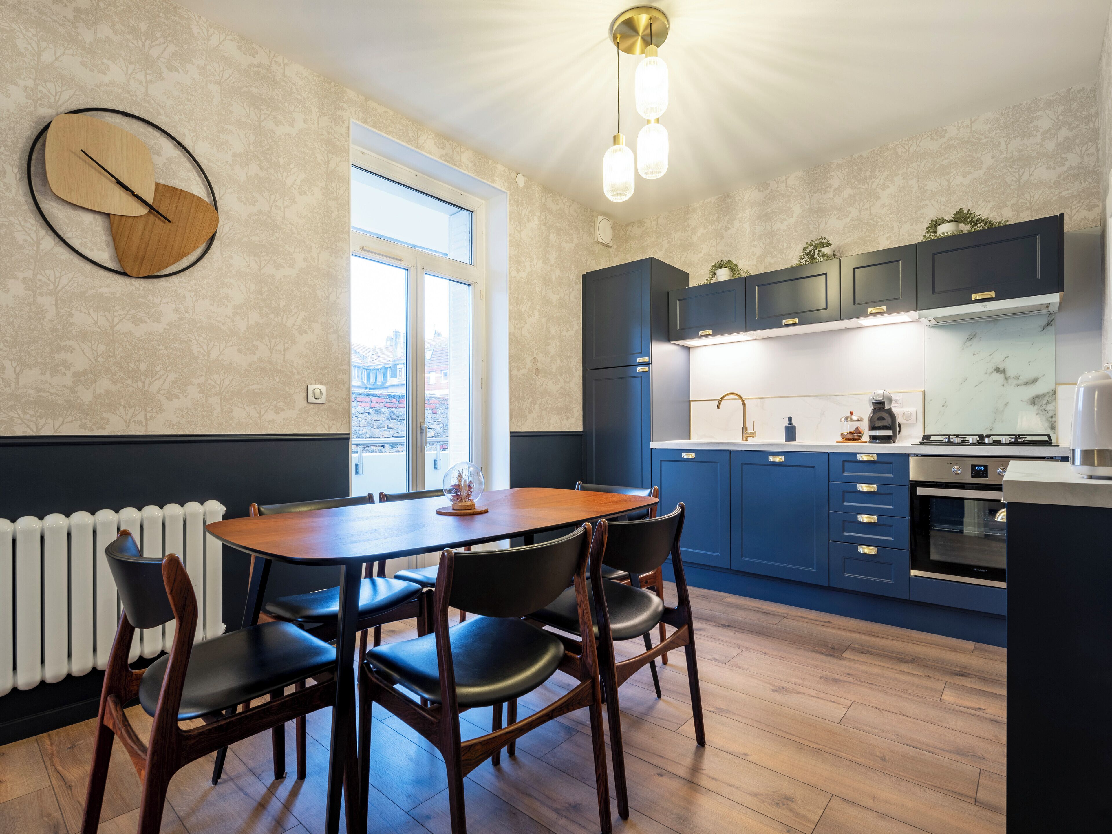 A modern kitchen with dark blue cabinets, a wooden dining table with chairs, and a large window.