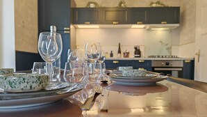 Una mesa de comedor dispuesta con cristalería transparente y platos estampados, con una cocina moderna al fondo.