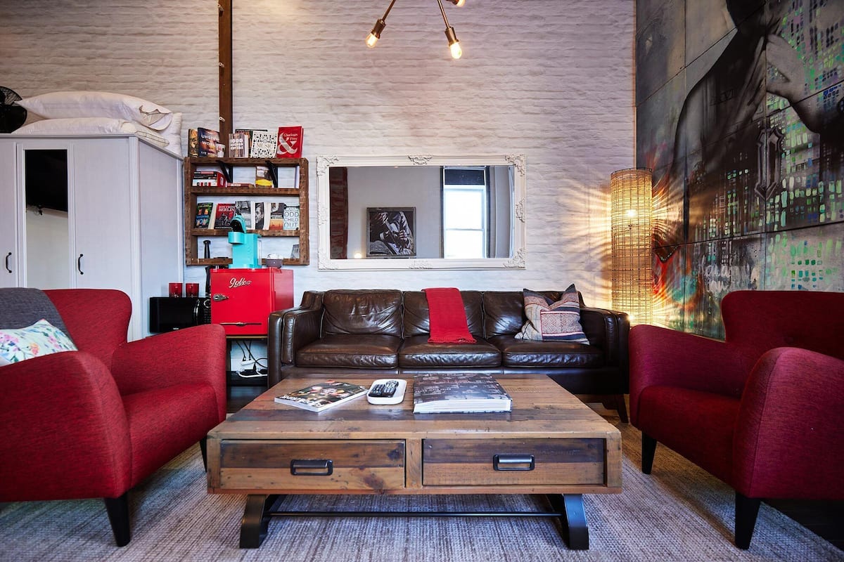 Una sala de estar moderna con un sofá de cuero, sillones rojos, una mesa de centro de madera con revistas, y una estantería llena de libros y revistas.