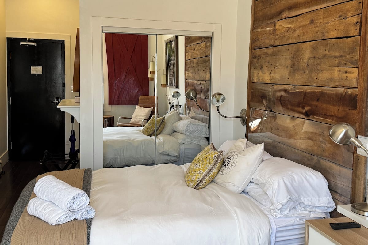 Una habitación de hotel con una cama grande, un cabecero de madera, un espejo y una mesita de noche con una lámpara.