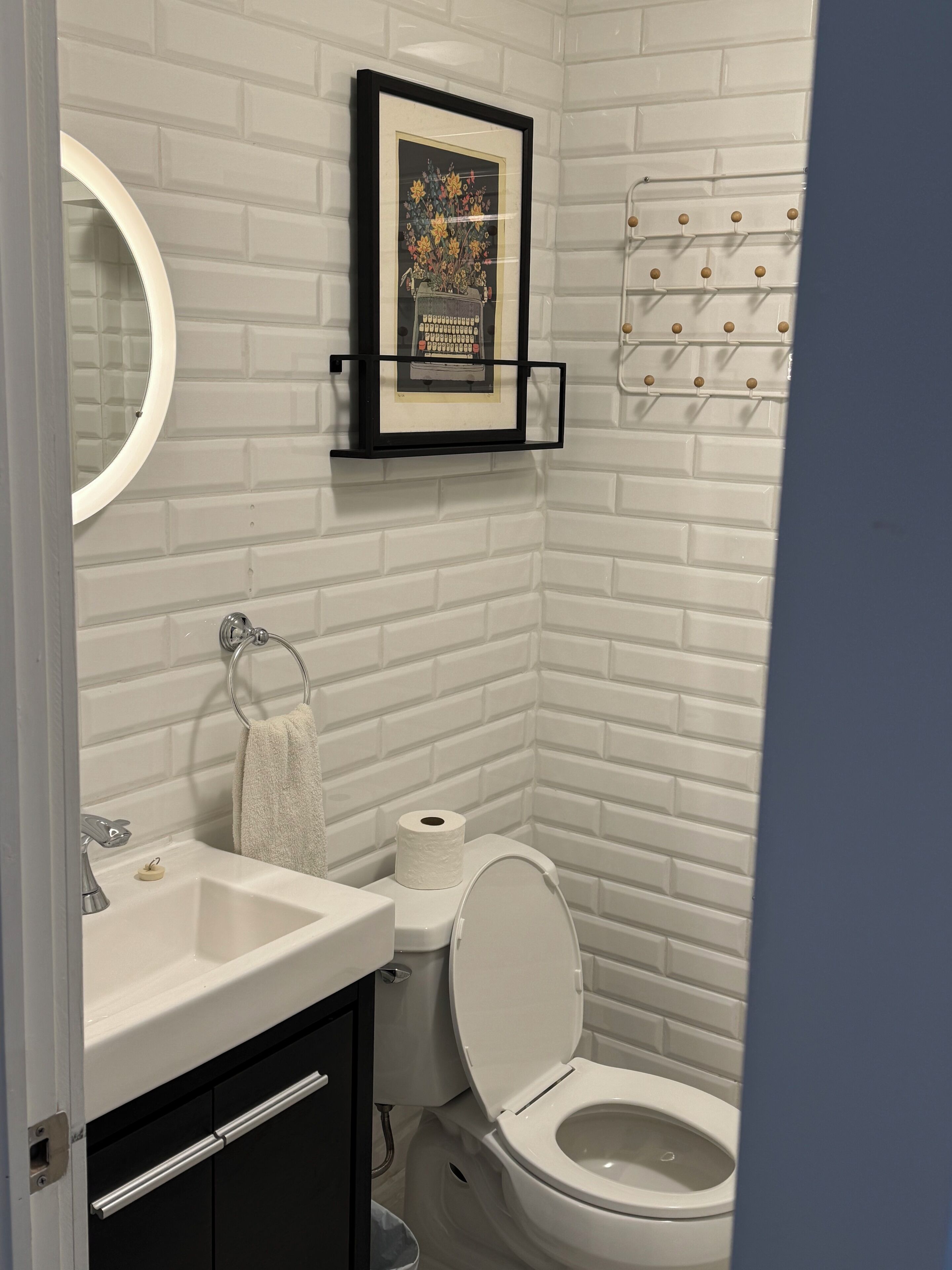 A bathroom with a white brick wall, a framed picture of a vintage typewriter, a toilet, and a sink with a faucet.