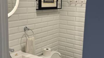 A bathroom with a white brick wall, a framed picture of a vintage typewriter, a toilet, and a sink with a faucet.