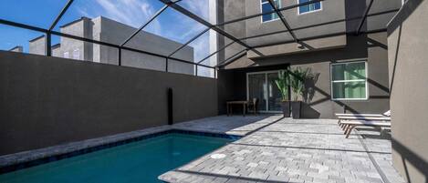 A swimming pool with a brick patio, a covered outdoor seating area, and a modern building with large windows.