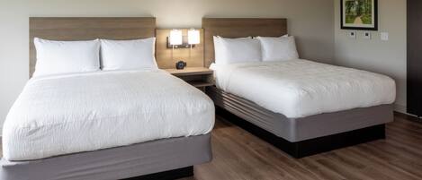 A hotel room with two beds, a nightstand, and a wall-mounted light fixture.