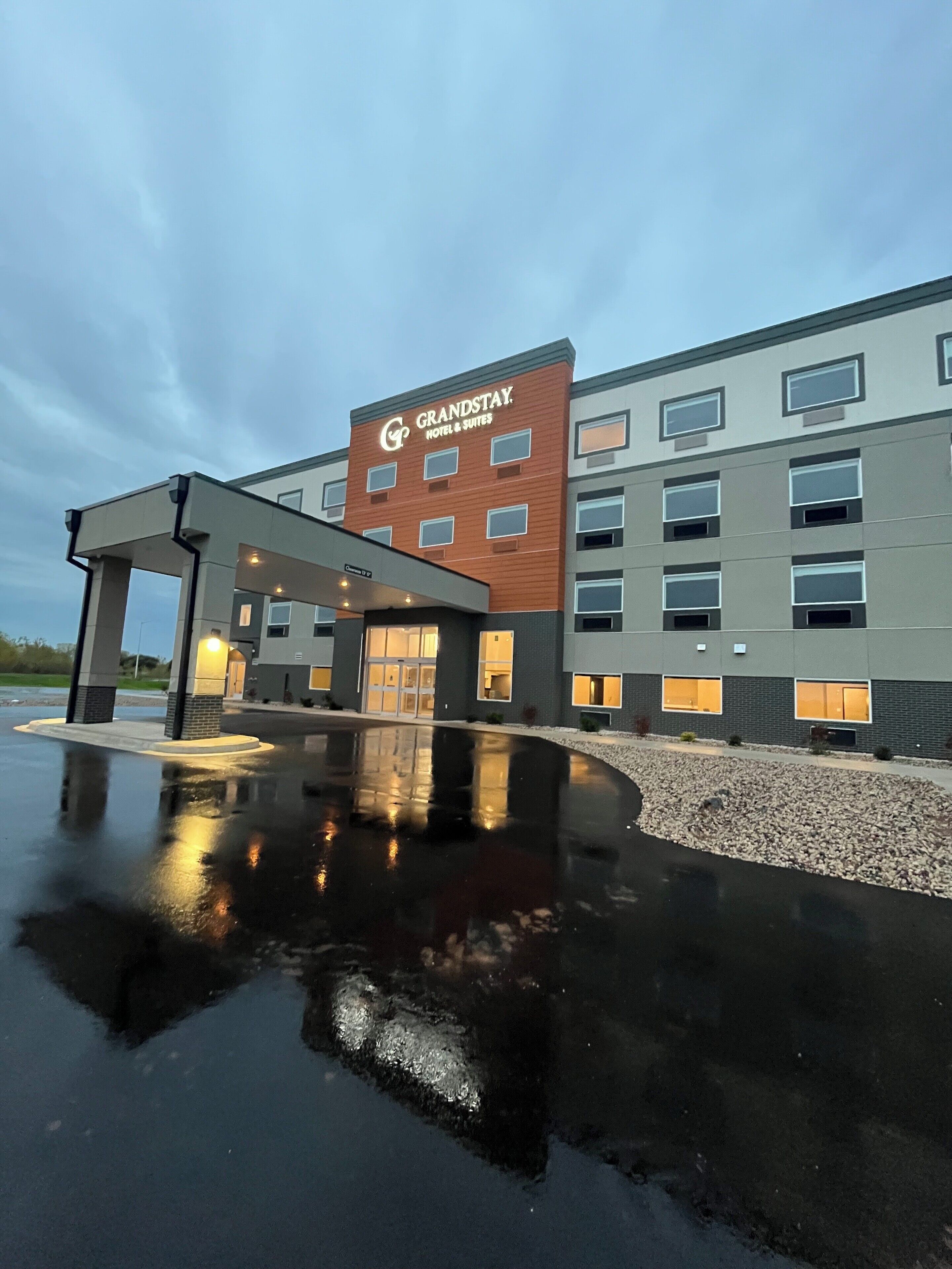 A modern hotel with a prominent 'GrandStay Hotel & Suites' sign, a covered entrance, and a wet reflective ground.