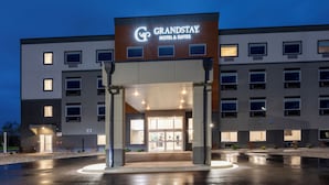 Een GrandStay Hotel & Suites gebouw met een modern ontwerp, met een opvallende ingang met glazen deuren en een overdekte doorgang.