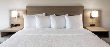 A neatly made bed with white bedding and a wooden headboard. There are two bedside tables with lamps and a digital clock on one.