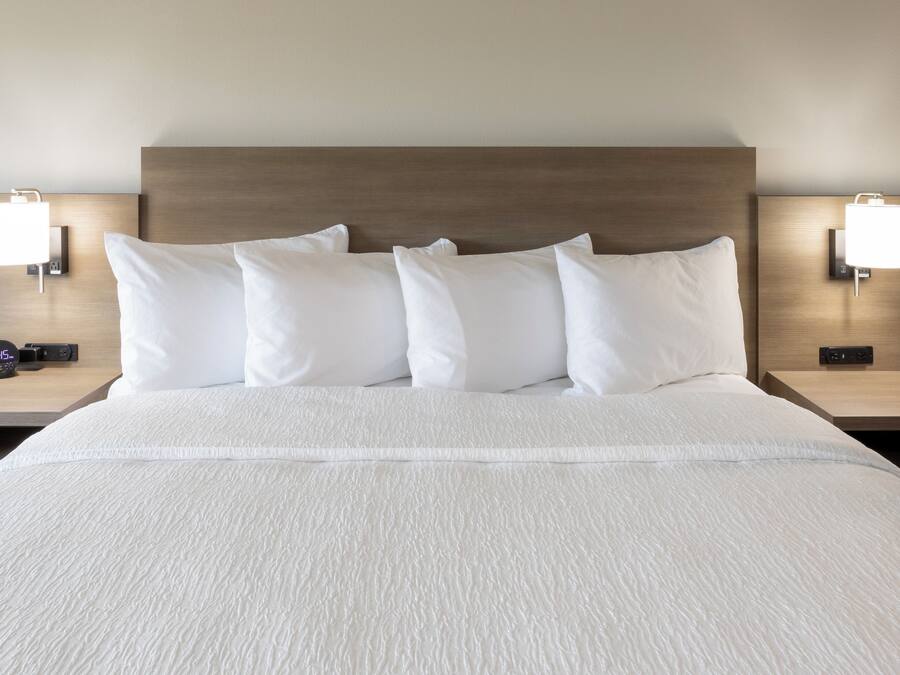 A neatly made bed with white bedding and a wooden headboard. There are two bedside tables with lamps and a digital clock on one.