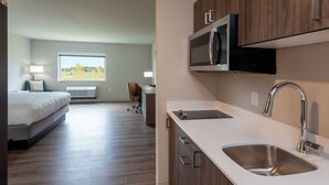 Een modern appartement met een keuken, inclusief een roestvrijstalen spoelbak, een magnetron en houten kastjes. Een groot raam biedt uitzicht op de omgeving.