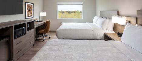 A hotel room with a large bed, a desk with a chair, a TV, and a window with a view of trees.