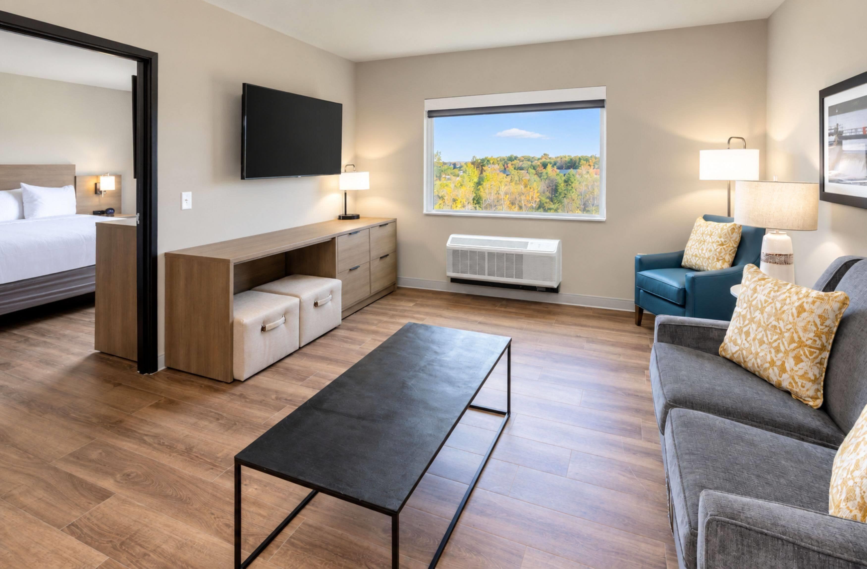 A hotel room with a bed, a desk, a TV, a window with a view, a sofa, and a coffee table.