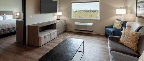 Habitación de hotel moderna con cama, escritorio, sofá y ventana grande con vista a árboles.