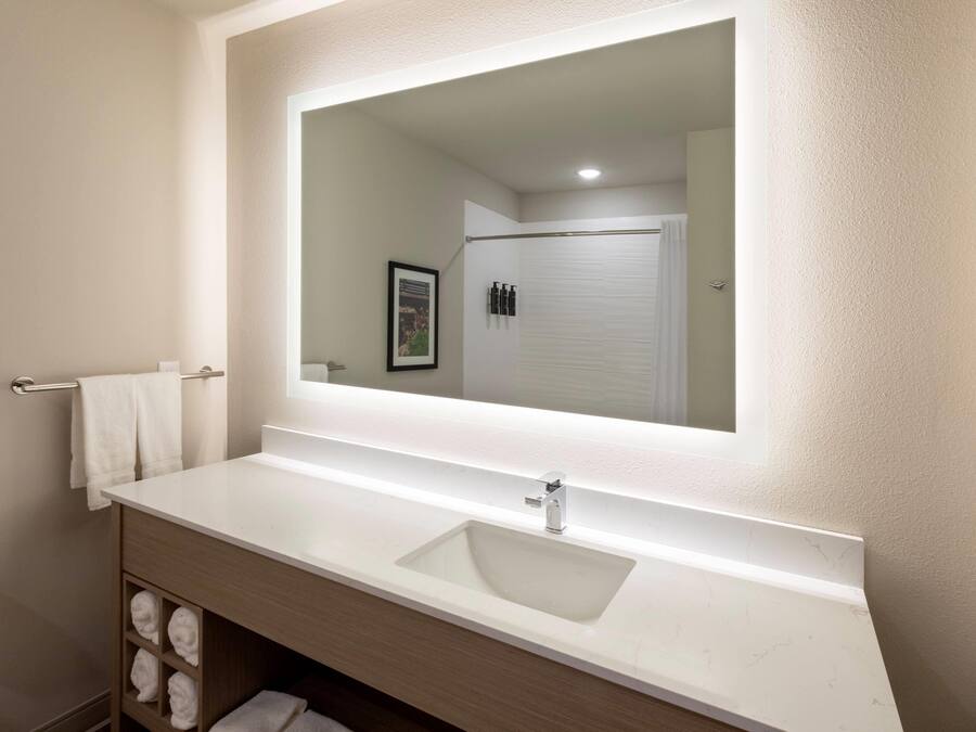 Un baño con tocador blanco, un espejo grande y un perchero para toallas.