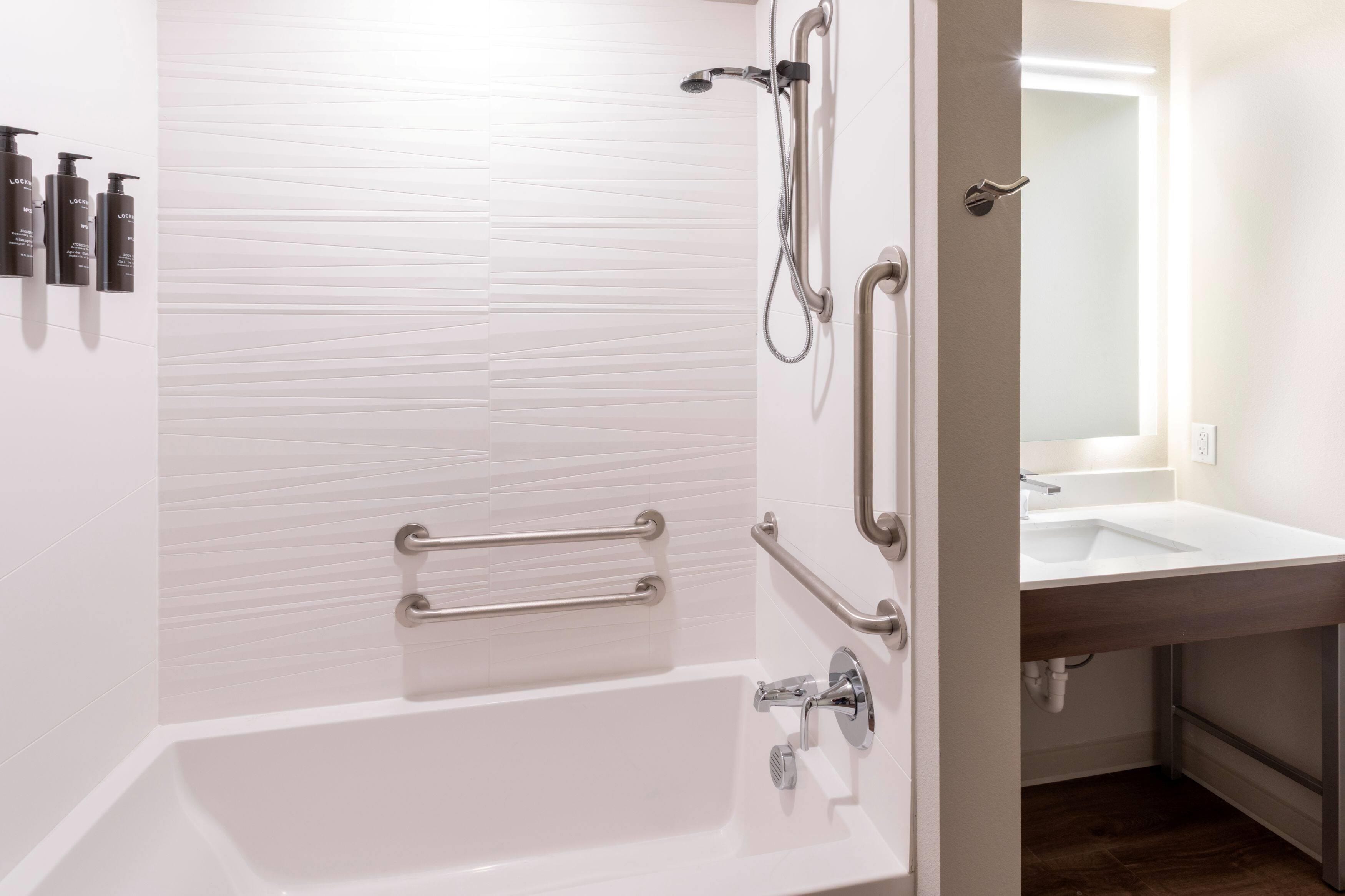 Ein modernes Badezimmer mit einer weißen Badewanne, einer Dusche inklusive Handbrause und einem Waschtisch.