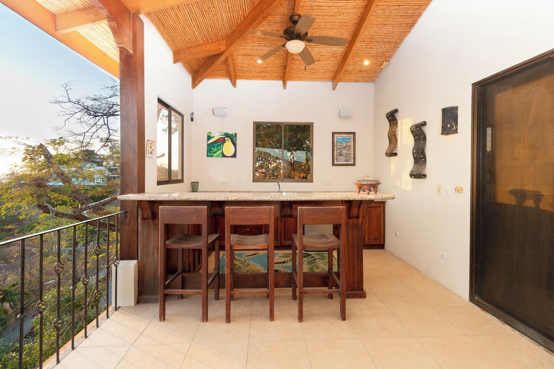A balcony with a wooden ceiling, a bar area with stools, and artwork on the walls.