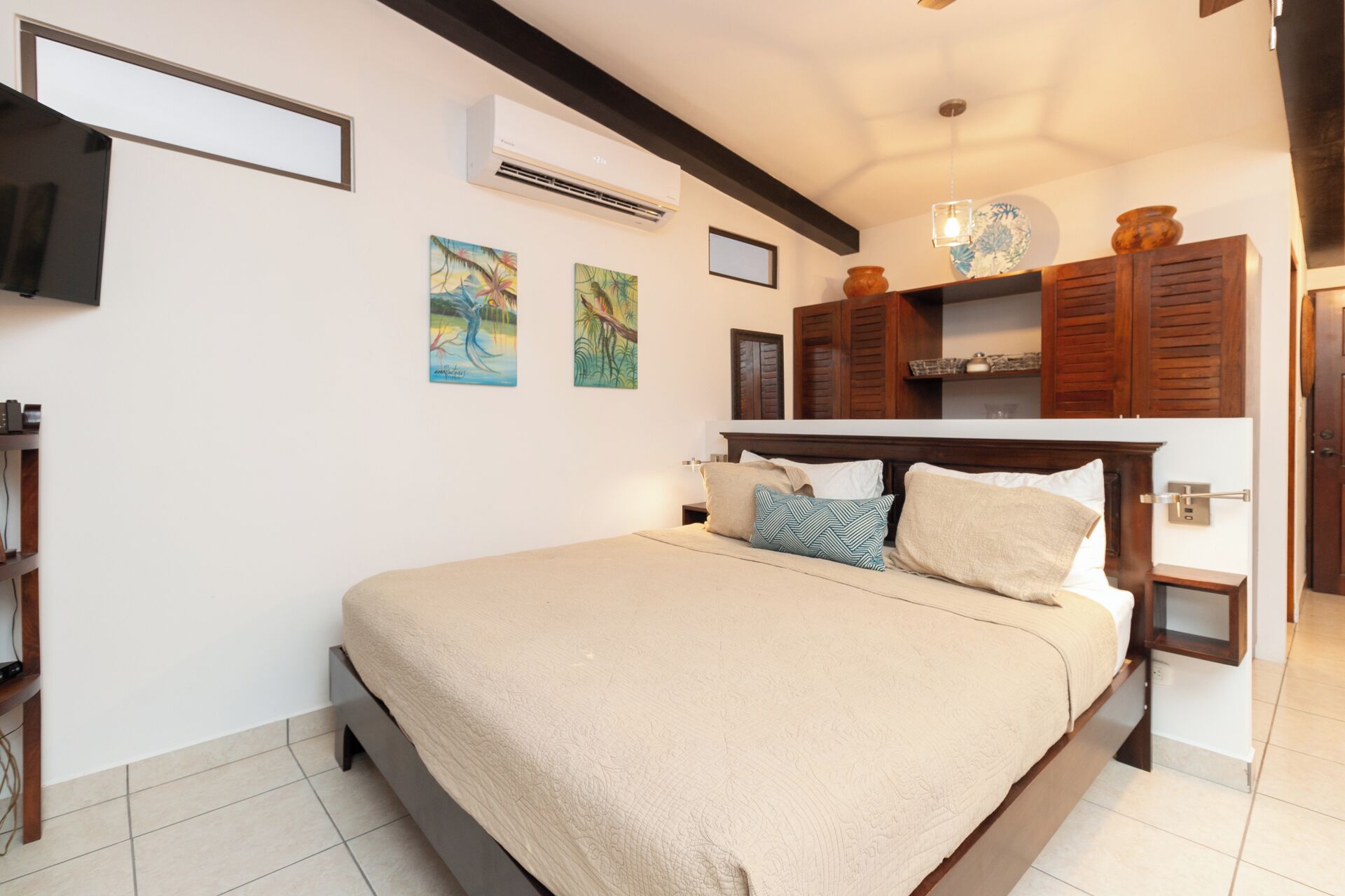 Quarto com cama, televisão na parede, ar condicionado e obras de arte nas paredes.