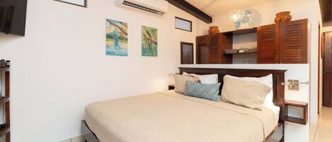 Quarto com cama, televisão na parede, ar condicionado e obras de arte nas paredes.
