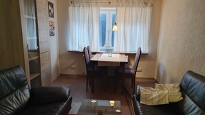 Un salon avec une table basse en verre, deux canapés en cuir noir, une table à manger avec des chaises et une fenêtre avec des rideaux.