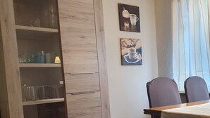 Un coin repas avec une table et des chaises en bois, un meuble en bois doté d’étagères, et deux tableaux accrochés au mur.