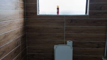 Ein Badezimmer mit Holzwänden, einer Toilette, einem Fenster und einer Toilettenpapierrolle.