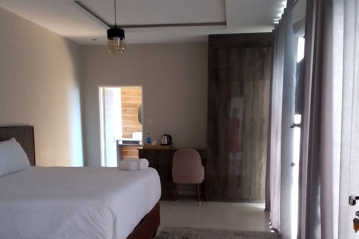 A hotel room with a large bed, a desk, a chair, and a view of the outside.