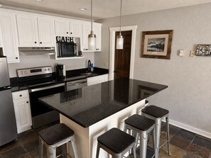 A kitchen with white cabinets, a black countertop, stainless steel appliances, and a bar stool seating area. - The Powder Haven Chalet (Park City)