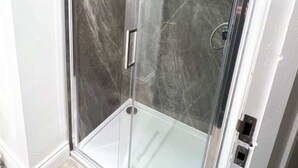 Une cabine de douche fermée par des parois en verre, avec un mur qui ressemble à du marbre.
