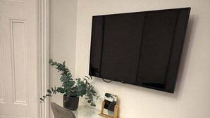 Un bureau blanc avec une chaise, une plante en pot, un miroir et un téléviseur fixé au mur.