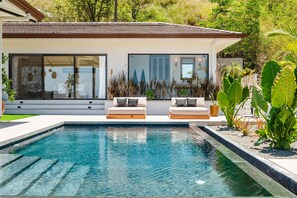 Ett modernt hus med en swimmingpool, utomhusmöbler och frodig grönska.